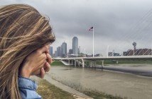 Stock photo of a woman with her face buried in her hand standing by a city waterfront