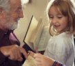 Older person pointing out a page in the Bible to two smiling young children