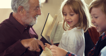 Older person pointing out a page in the Bible to two smiling young children