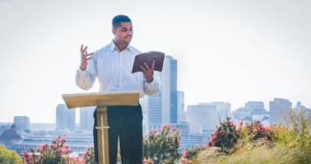 Person preaching outside with a city skyline in the background