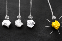 Wadded up paper representing light bulbs in a Newton's cradle. Three are white, and one is yellow, representing an idea. The yellow one is pulled back.